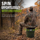 A man in camouflage sits on a green bucket outdoors in a wooded area, demonstrating a product with text overlays that read 'SPIN EFFORTLESSLY WITH ONE FINGER' and '360° Silent ball-bearing design for smooth, hands-free movement.'.
