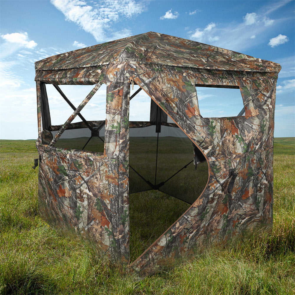 Camouflage hunting blind in a grassy field with a blue sky.